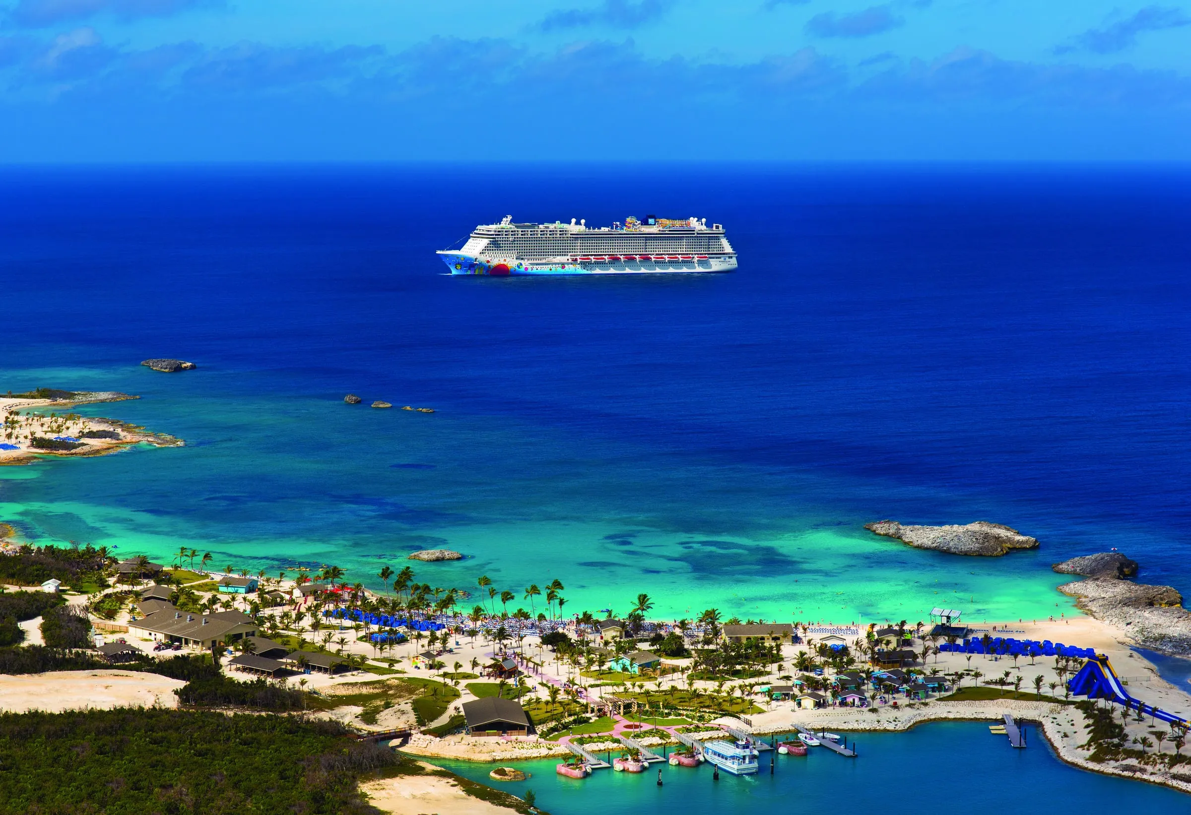 A cruise ship anchored in turquoise water off a small Caribbean island with a palm-lined beach